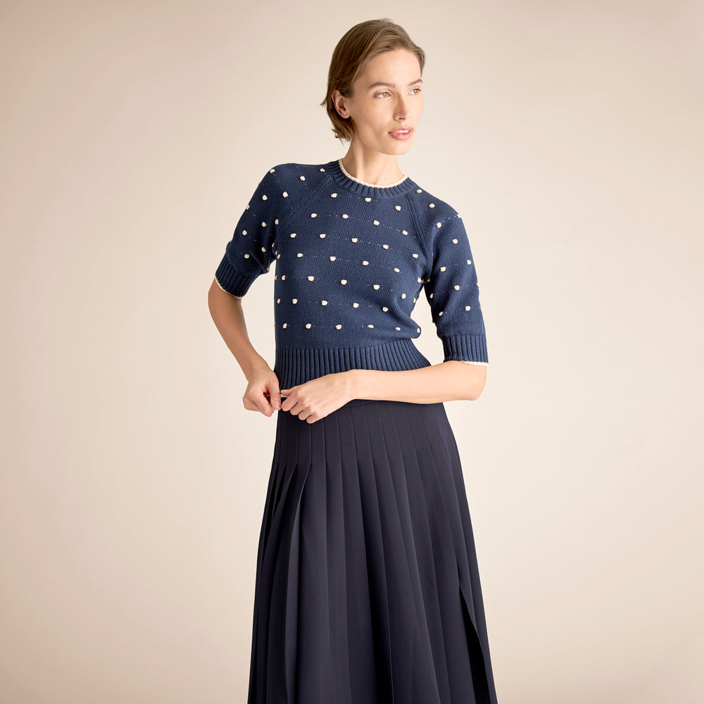 Woman wearing a navy sweater with white polka dots and a matching skirt on a beige background