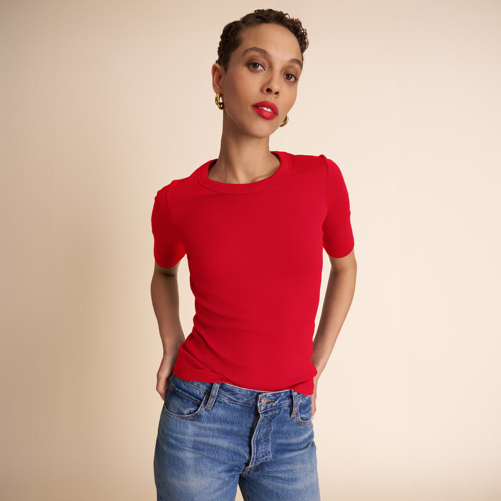 Woman wearing a red shirt and blue jeans against a beige background