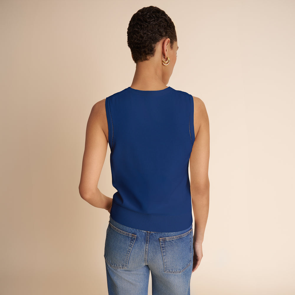 Person wearing a blue sleeveless top and jeans on a beige background