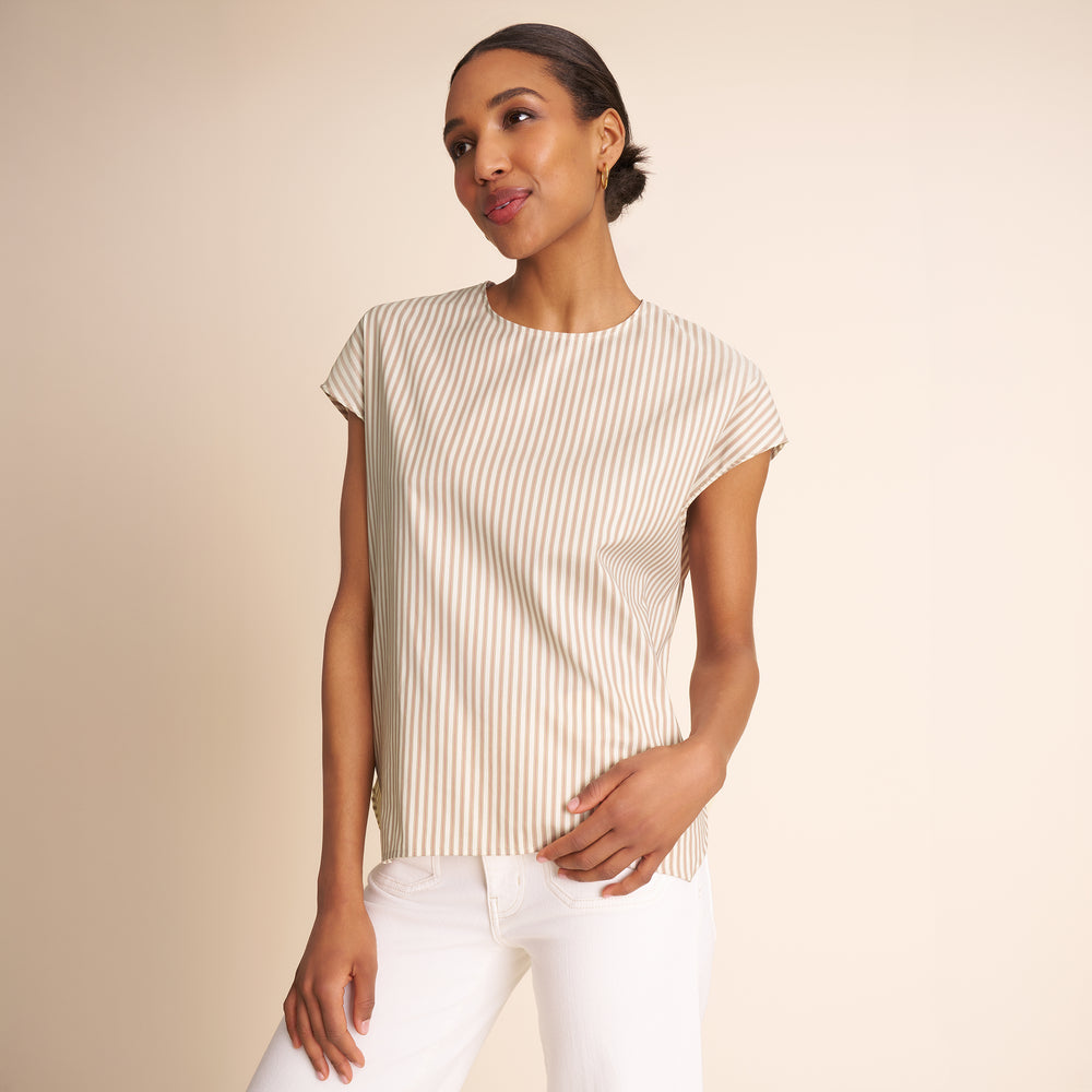 Woman wearing a striped shirt and white pants against a beige background.