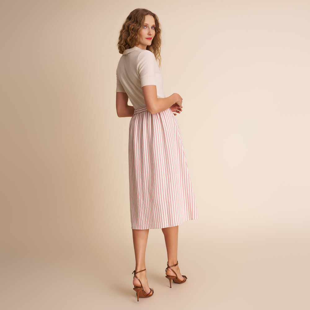 Woman wearing a white top and pink striped skirt on a beige background