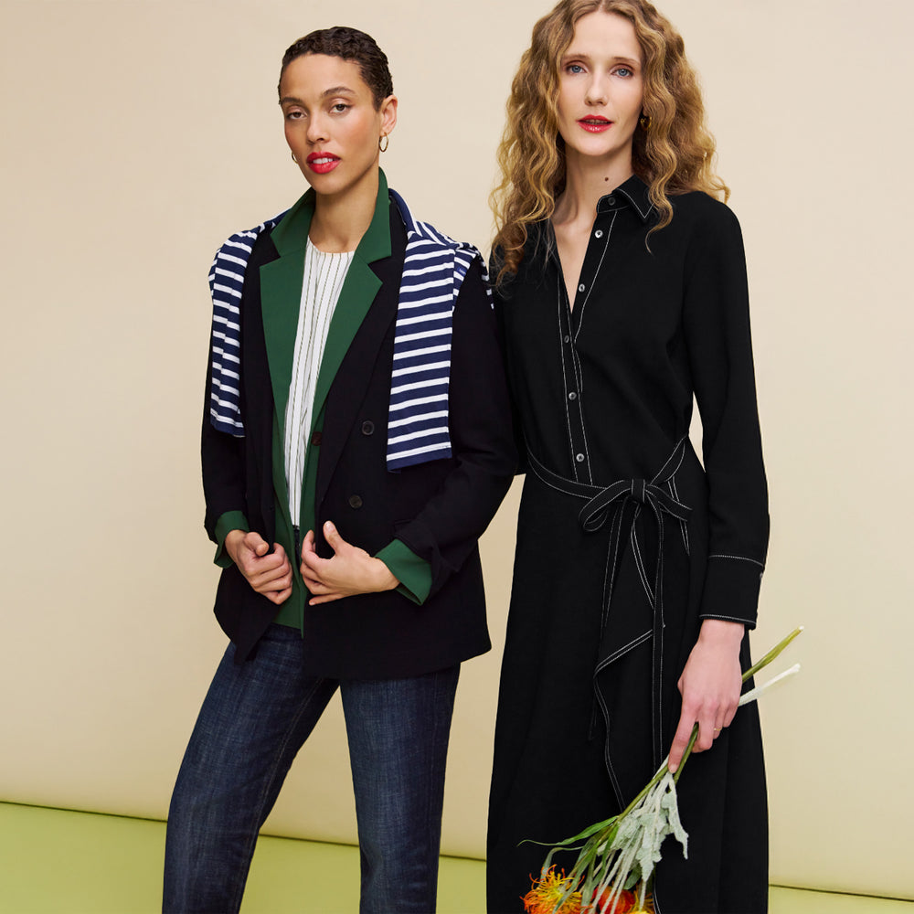 Two women standing side by side against a beige background, one wearing a striped jacket and the other in a black dress with a belt.