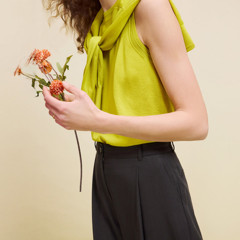 Person wearing a bright yellow sleeveless top and black pants, holding flowers against a beige background