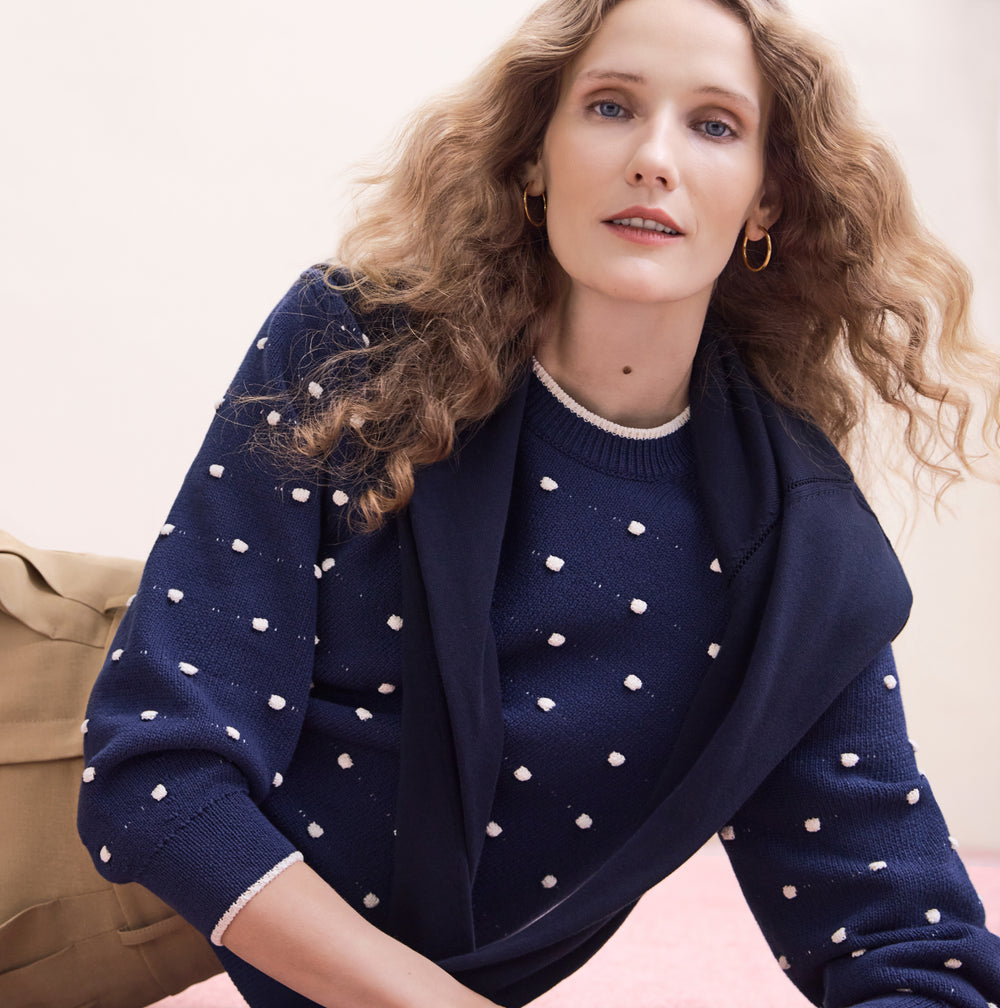 Person wearing a navy blue sweater with white polka dots on a beige background