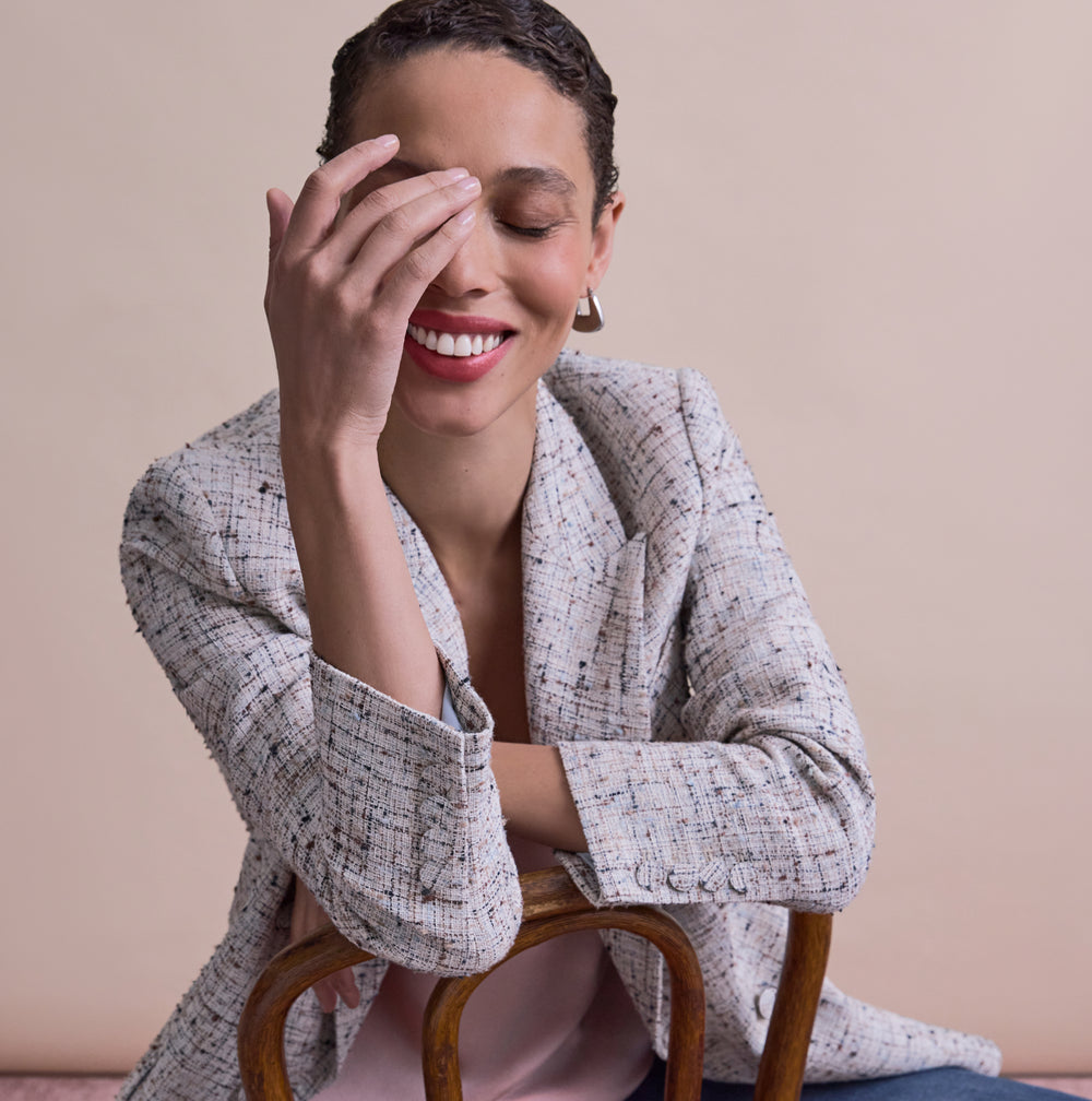 Woman sitting on a chair with one hand covering her face against a beige background