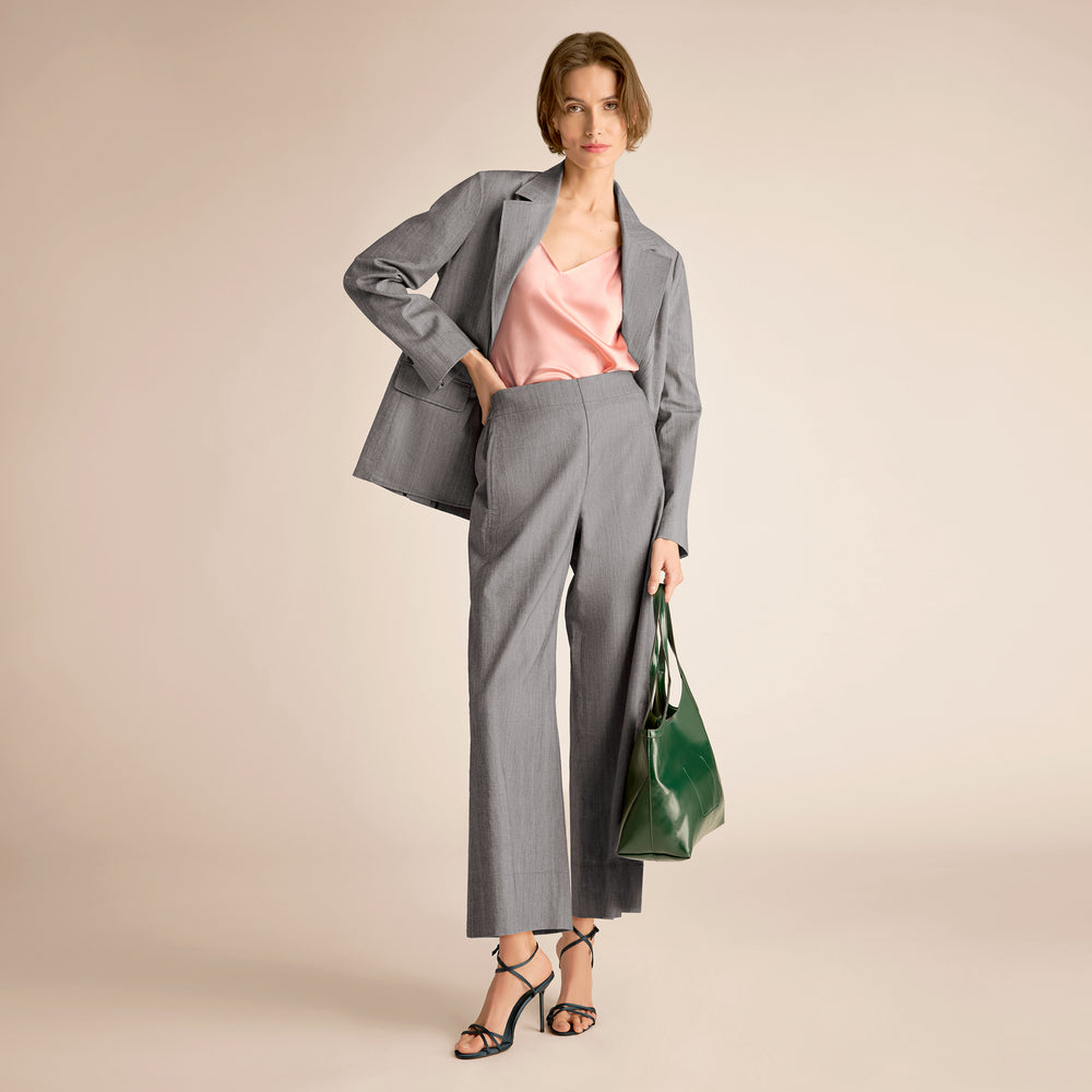 Woman in gray suit with pink top and green bag on beige background