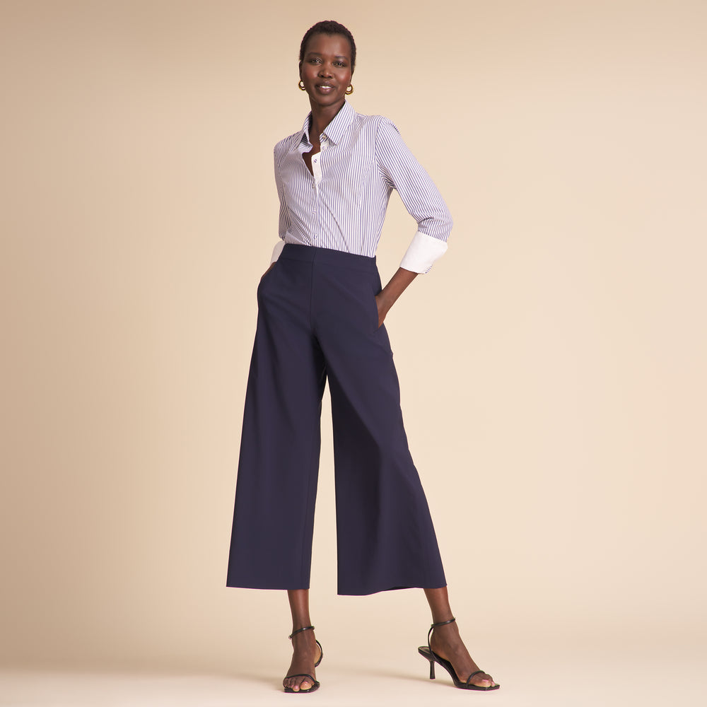 Woman wearing a white shirt with blue stripes and navy wide-leg pants on a beige background