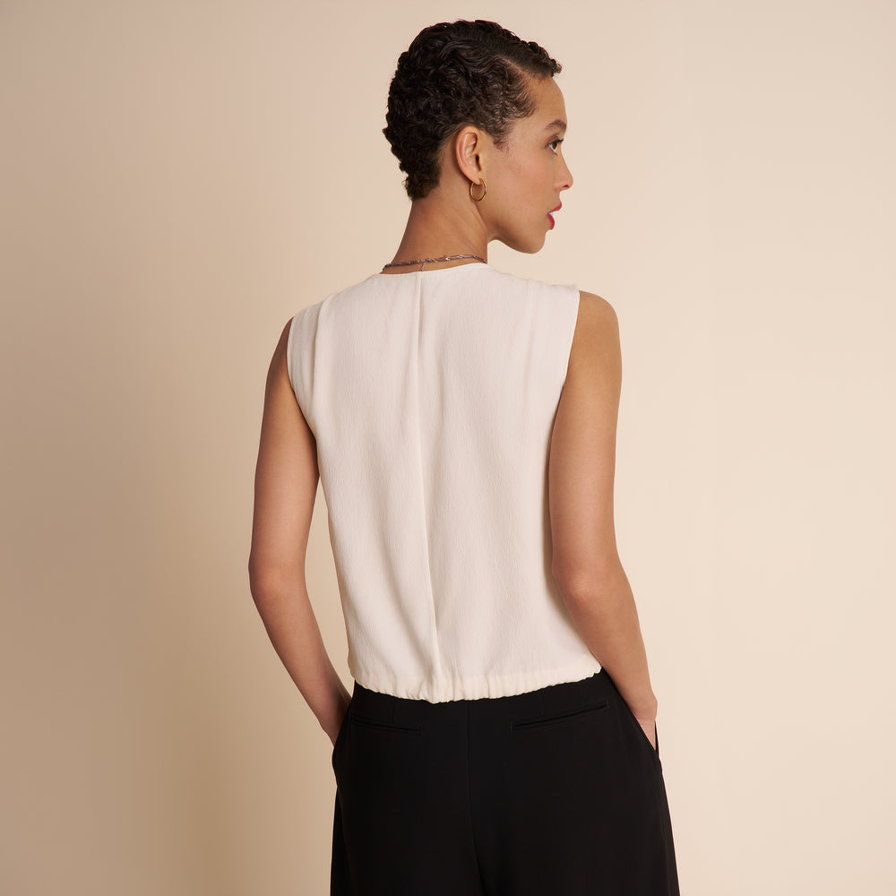 Woman wearing a white sleeveless top and black pants on a beige background
