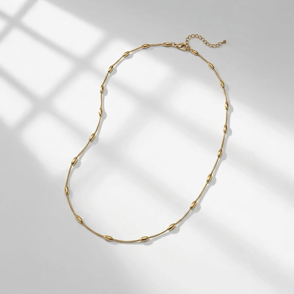 A gold chain necklace with elongated oval links, displayed on a light gray surface with soft window-box style shadows.