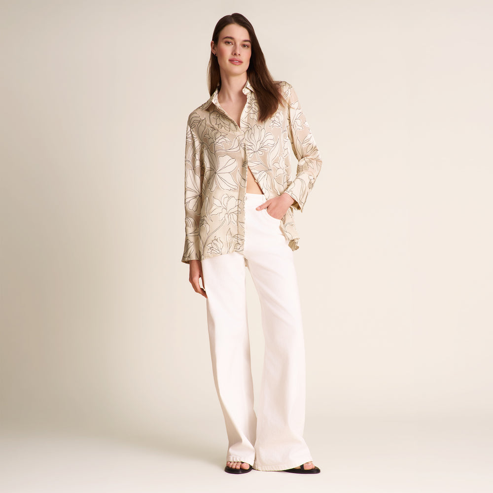 Woman wearing a patterned top and white pants on a plain background