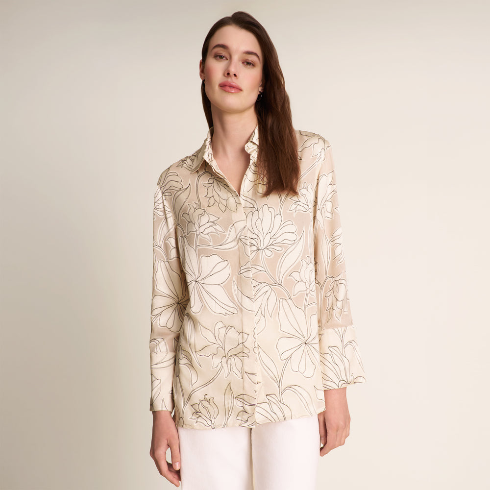 Woman wearing a beige floral patterned shirt against a plain background