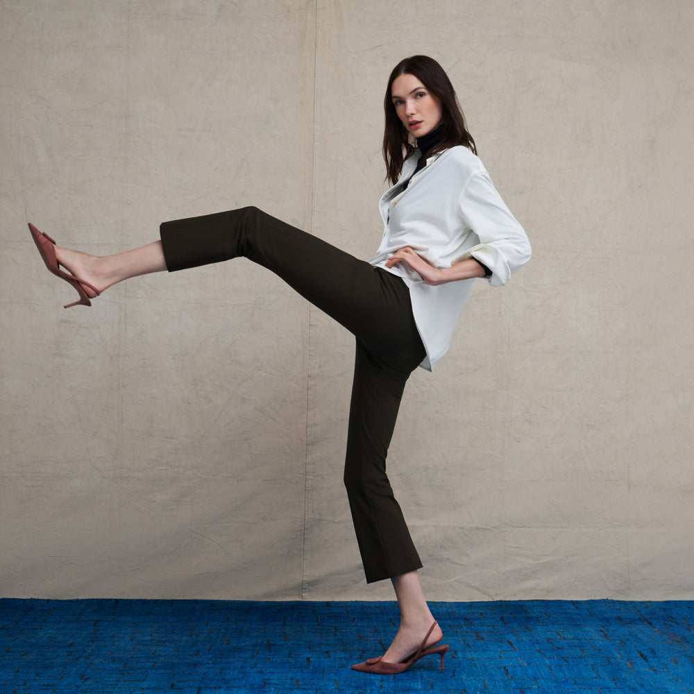 Woman wearing a white long sleeve button down and skinny black pants on a blue carpet floor and against a beige background