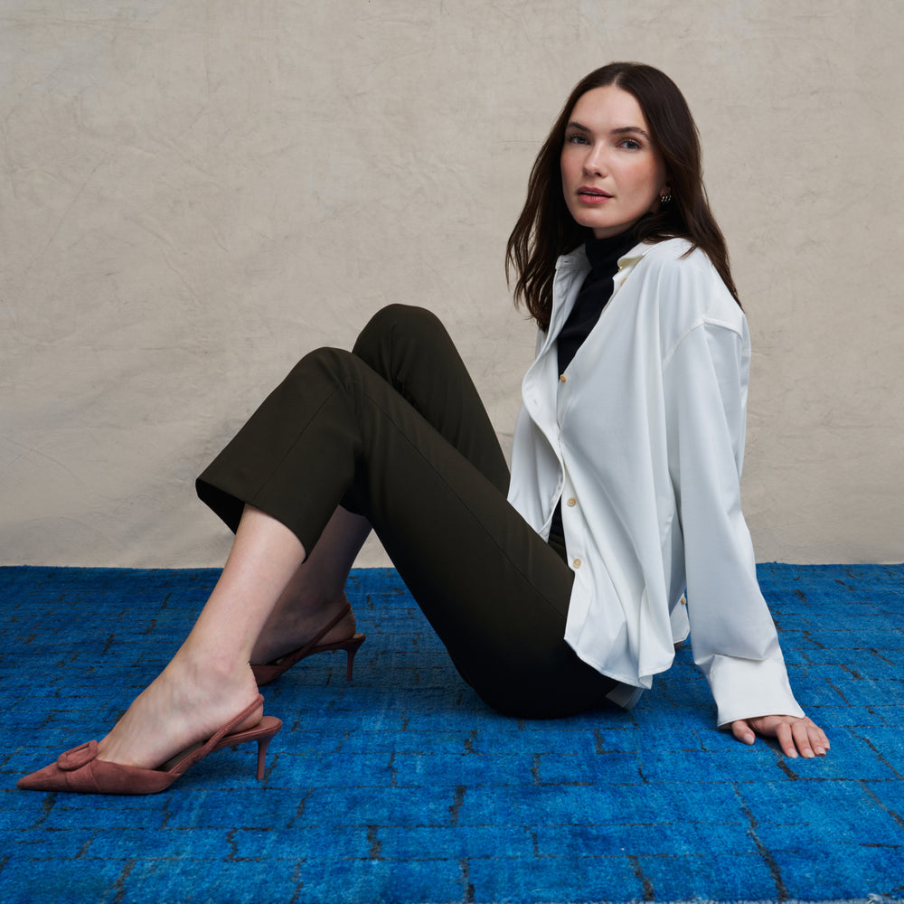 Woman wearing a white long sleeve button down and skinny black pants on a blue carpet floor and against a beige background