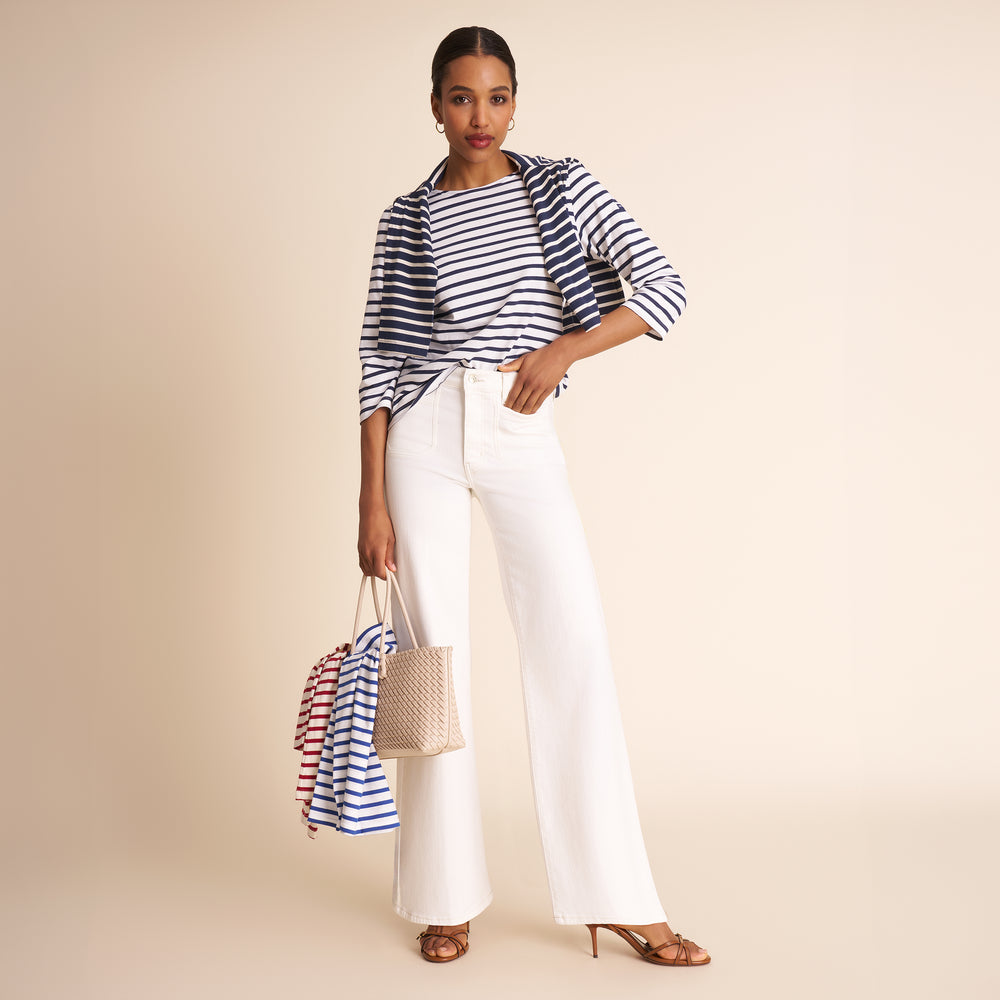 Woman wearing a striped shirt and white pants, holding bags against a beige background