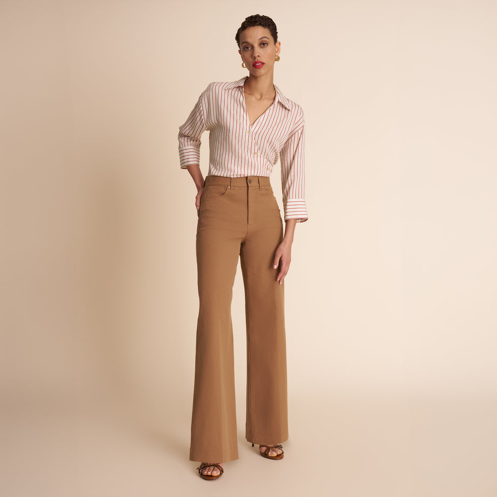 Woman wearing a striped shirt and tan pants on a beige background