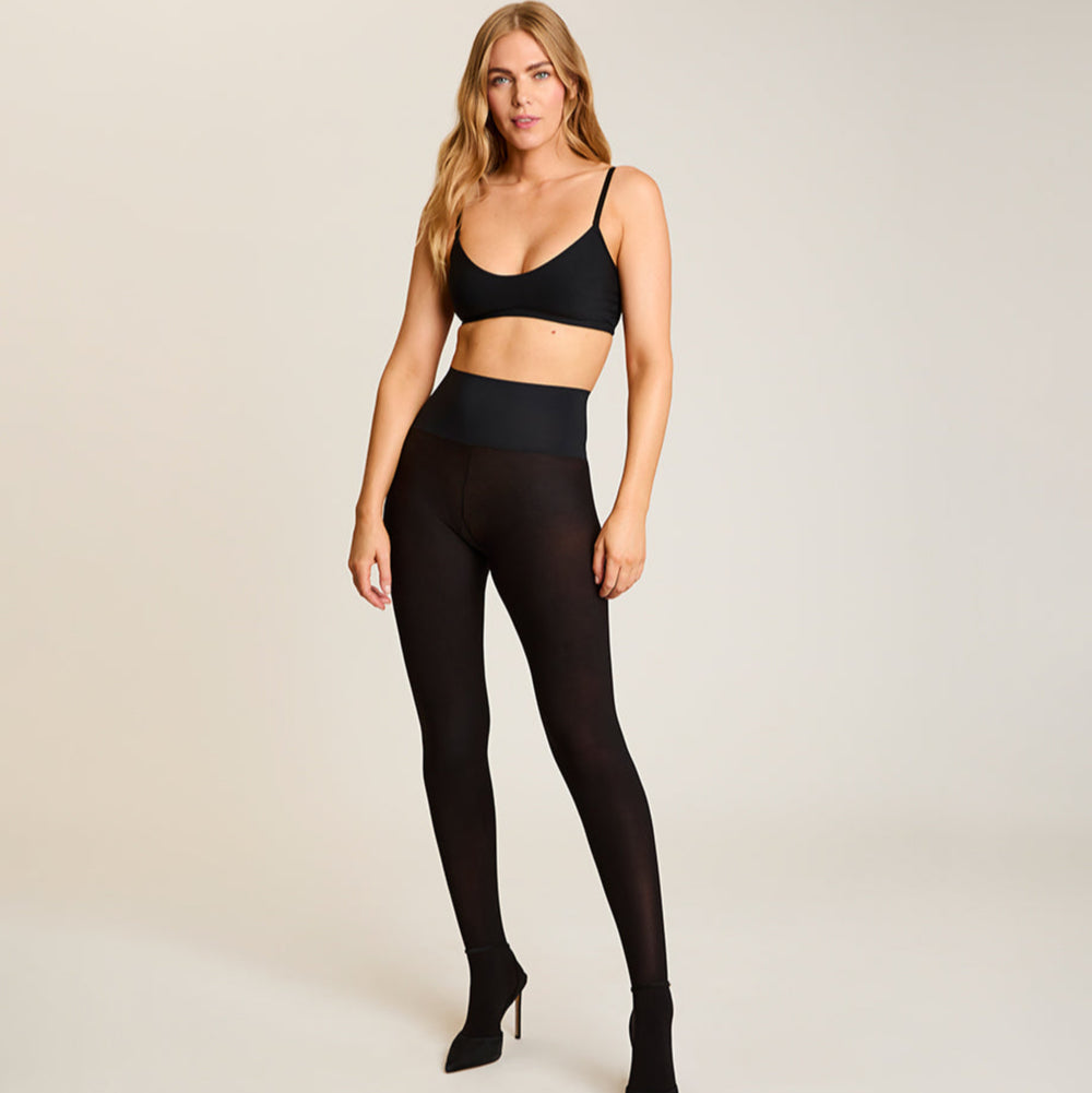 Woman wearing a black bra and tights on a plain background