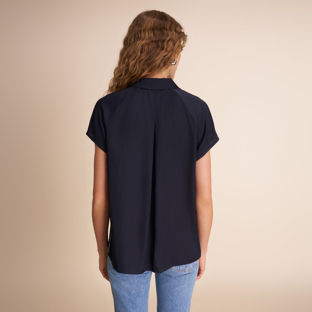 Person wearing a navy blue shirt and light blue jeans on a beige background