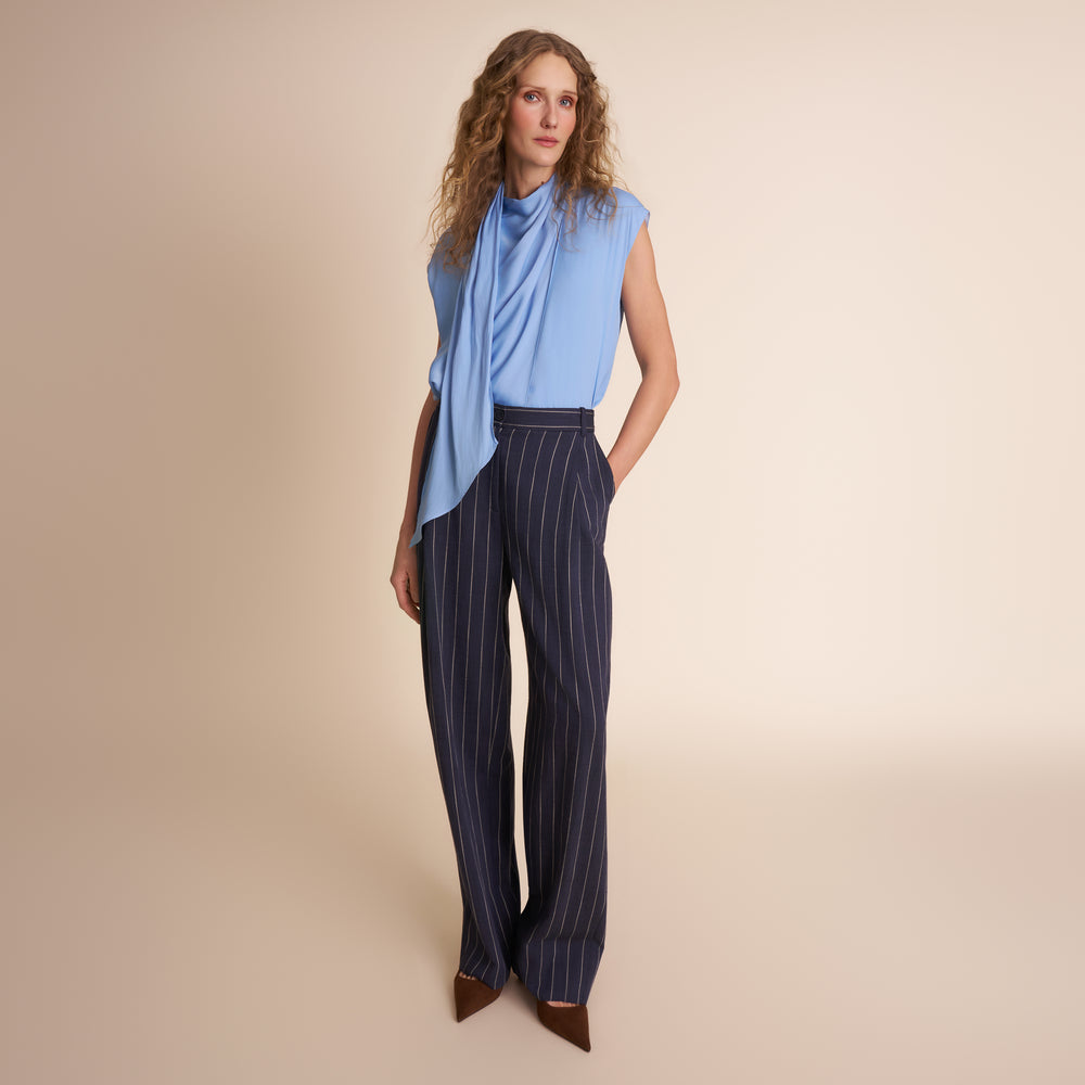 Woman wearing a blue sleeveless top and striped pants on a beige background