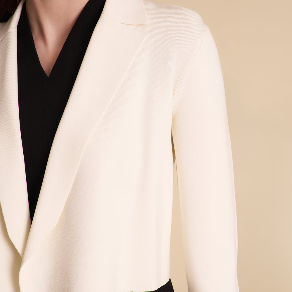 Woman wearing a white blazer over a black dress on a beige background