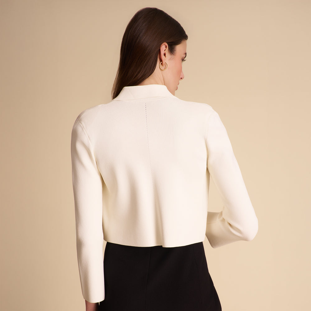 Woman wearing a white blazer over a black dress on a beige background