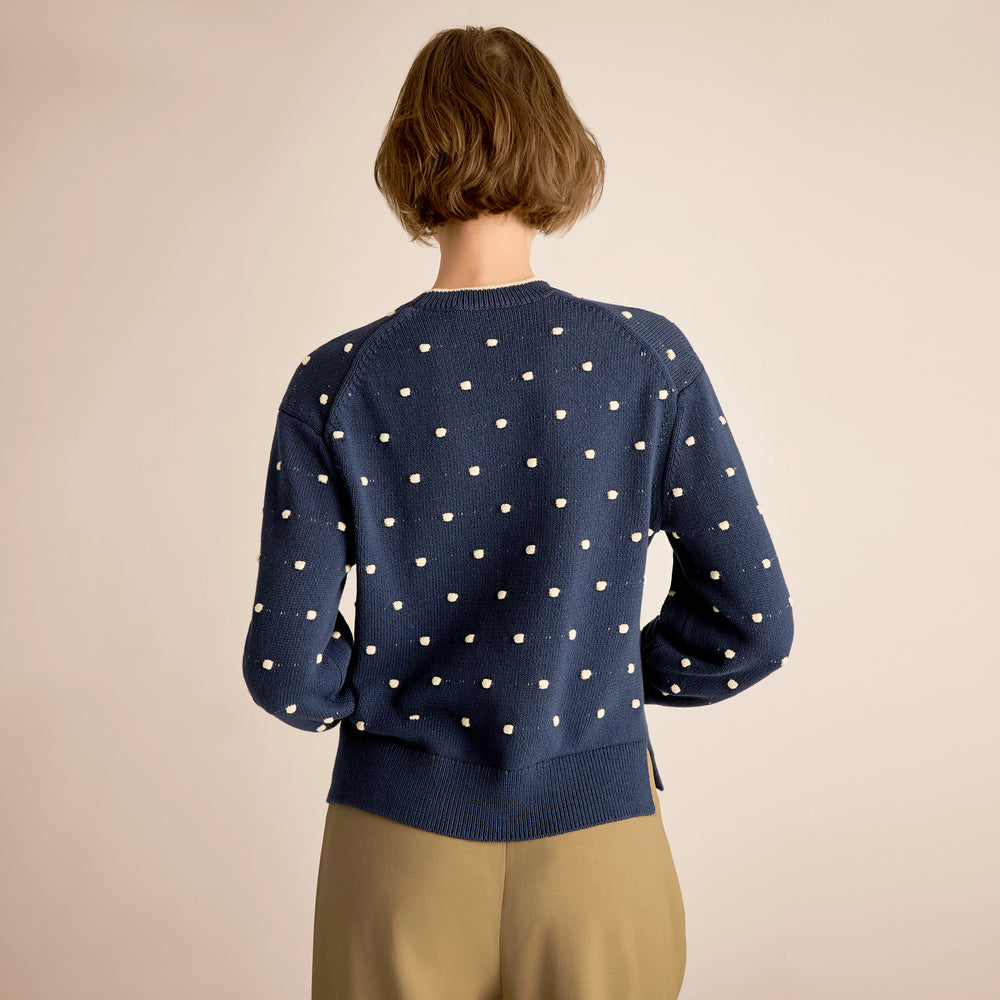 Person wearing a navy blue sweater with white polka dots on a beige background