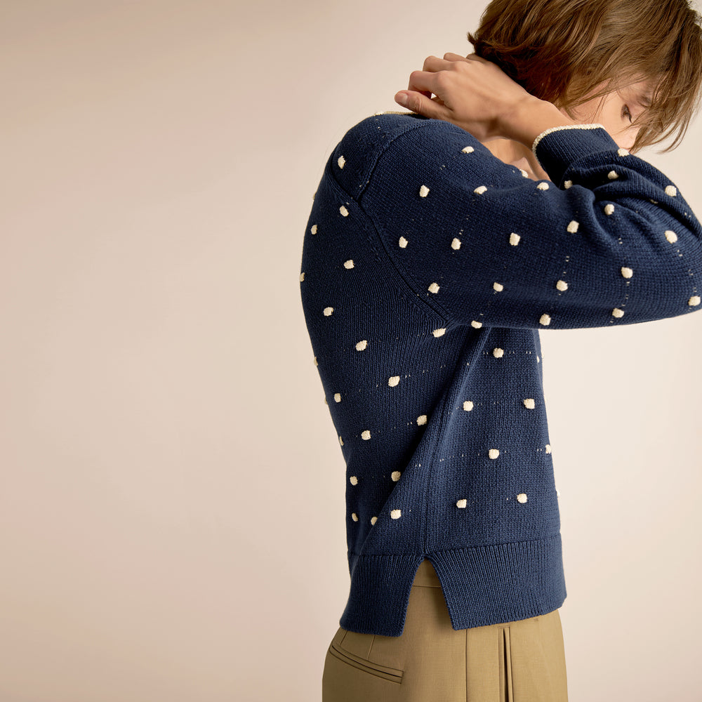 Person wearing a navy blue sweater with white polka dots on a beige background