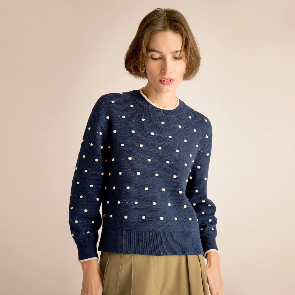 Woman wearing a navy blue sweater with white polka dots against a beige background