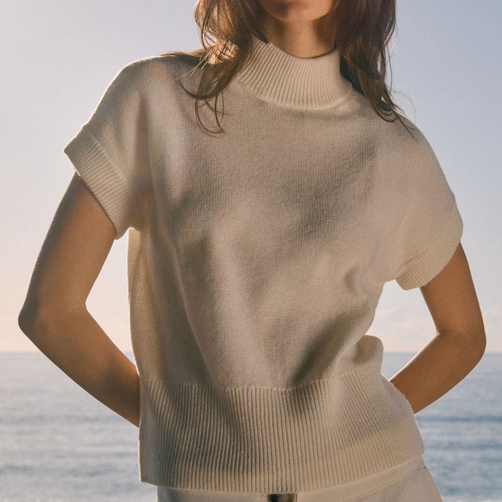 Person wearing a beige sweater and pants with a blurred ocean background
