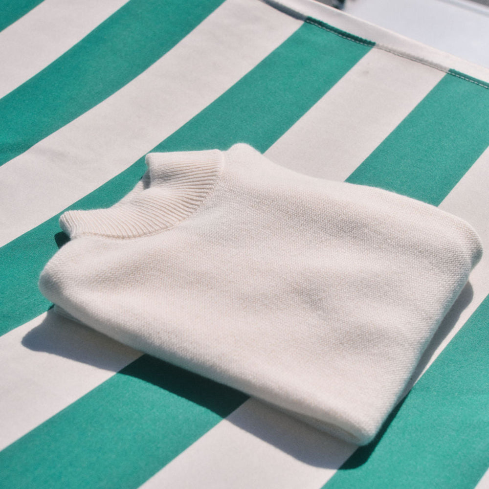 Folded white sweater on a green and white striped surface