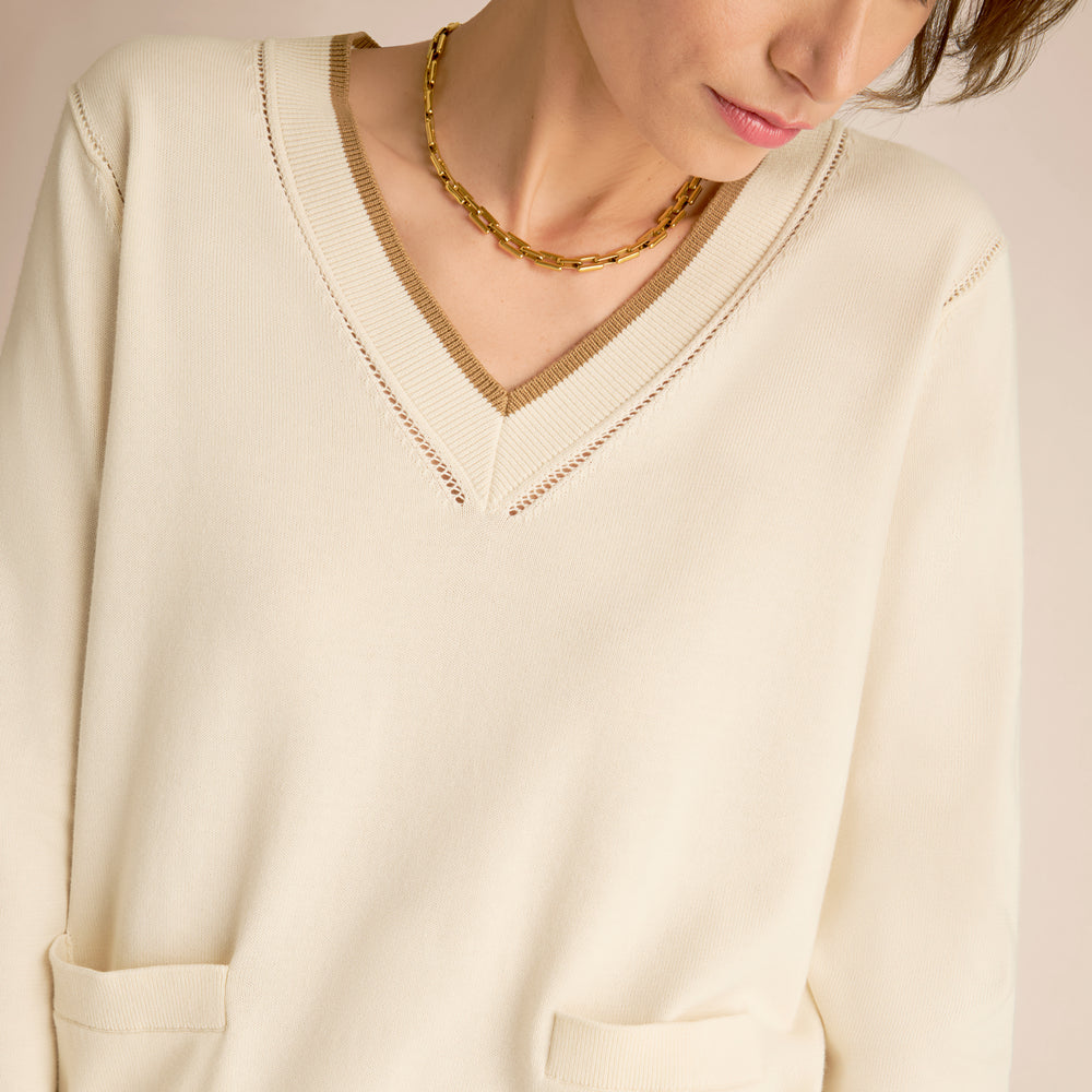 Close-up of a person wearing a cream-colored sweater with a gold necklace.