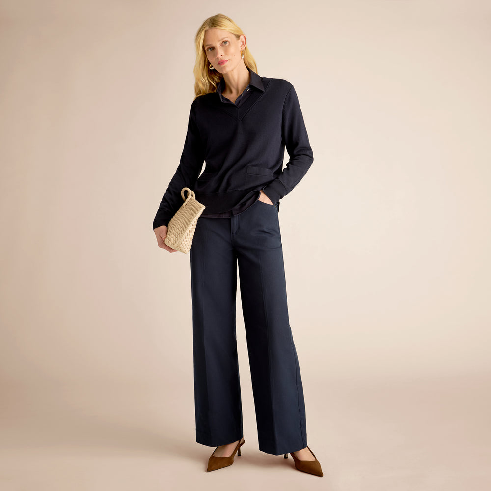 Woman wearing a navy outfit with wide-leg pants and holding a woven handbag on a beige background