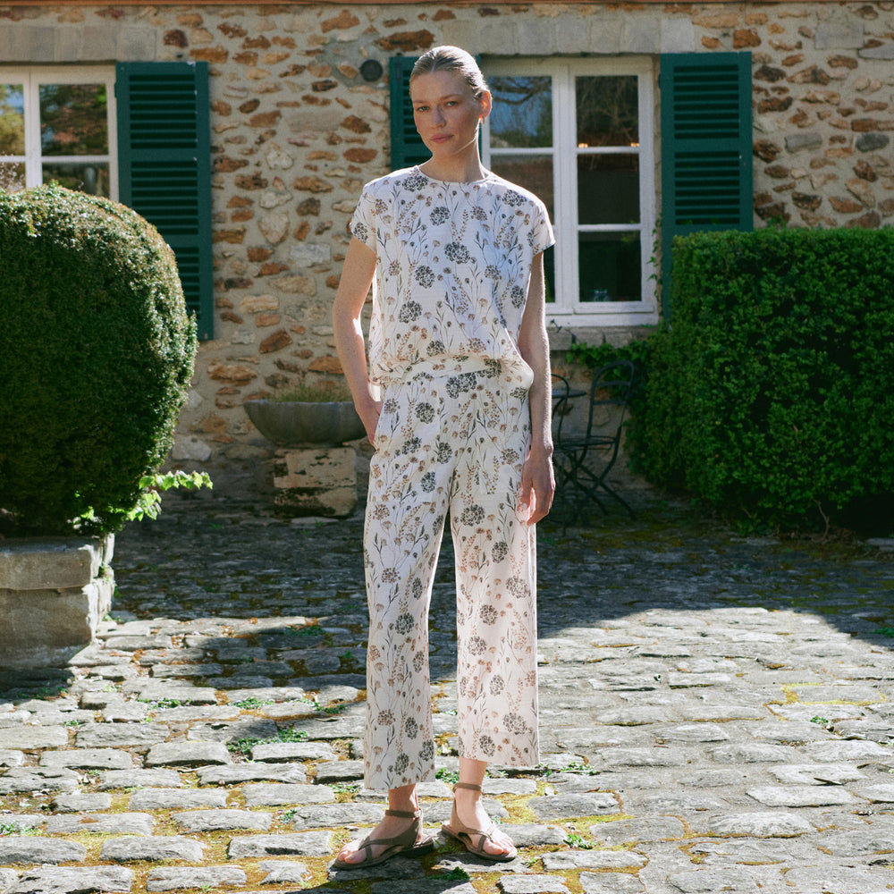 Woman in a floral outfit standing in front of a stone building with green shutters.