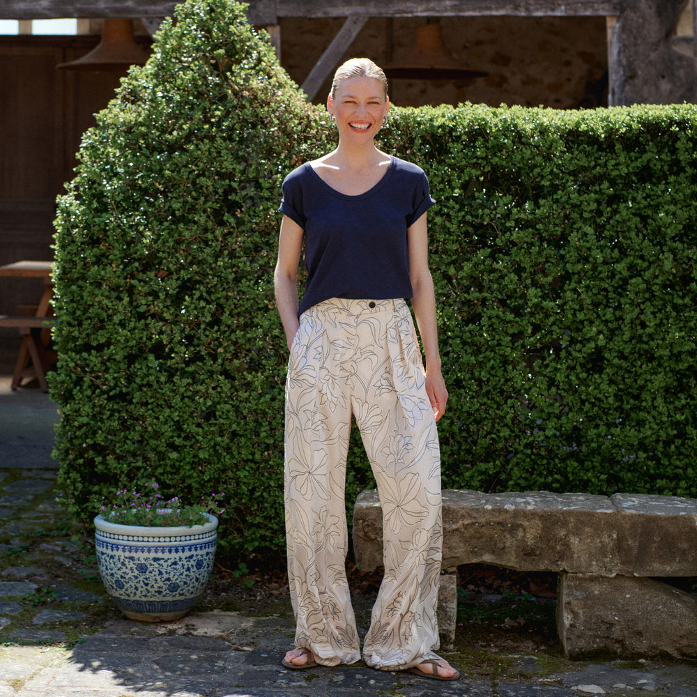 Woman standing outdoors in front of a hedge with a potted plant nearby