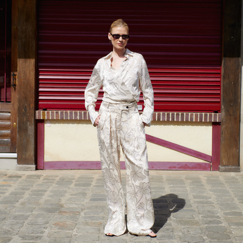 Woman in a white floral outfit standing in front of a red shutter.