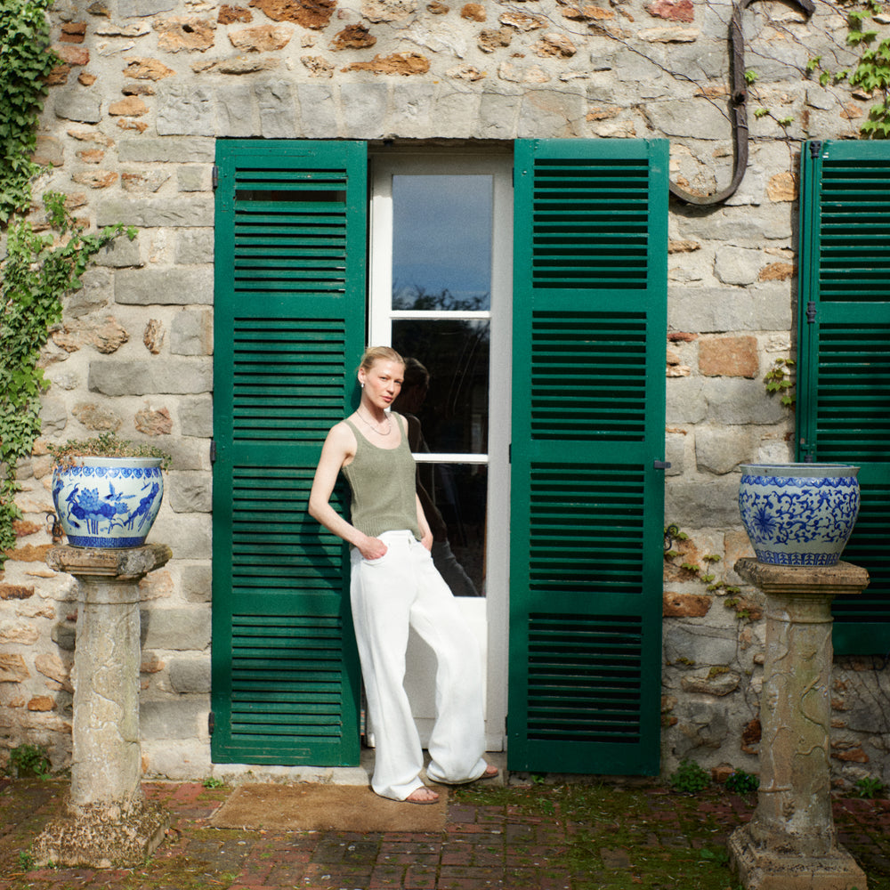 Woman standing in a doorway with green shutters and stone walls