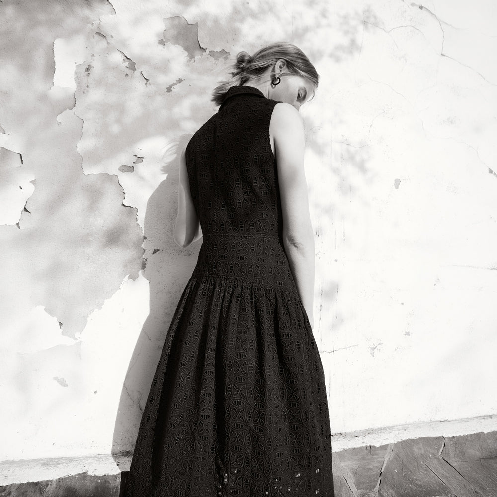 Woman in a black dress standing against a textured white wall.