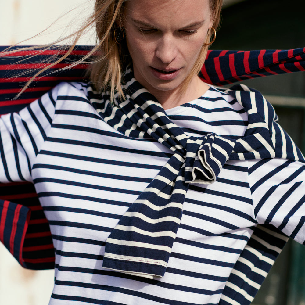 Woman wearing a striped shirt and scarf with a red and blue patterned chair in the background