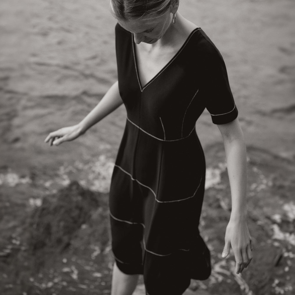 Woman wearing a black dress standing by a body of water.
