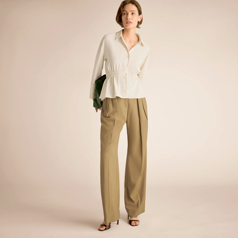 Woman wearing a white blouse and beige pants against a beige background