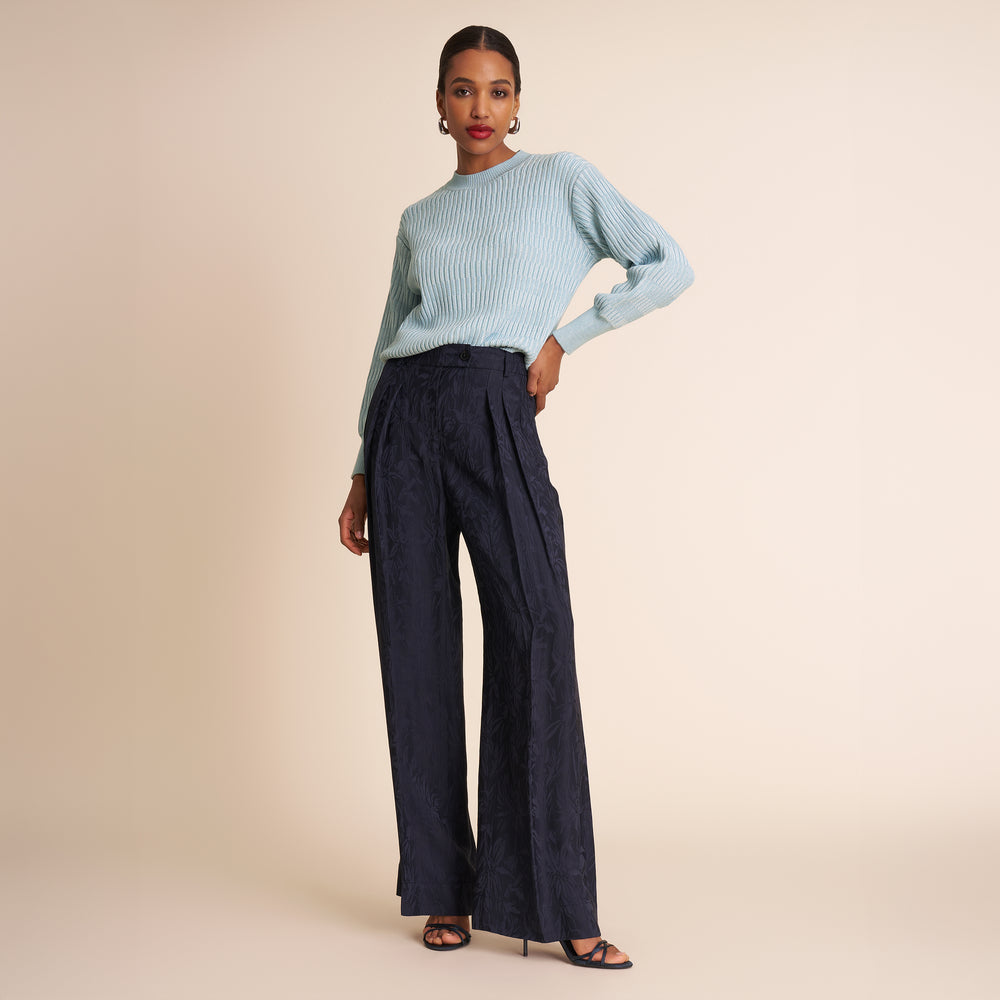Woman wearing a light blue sweater and dark pants on a beige background