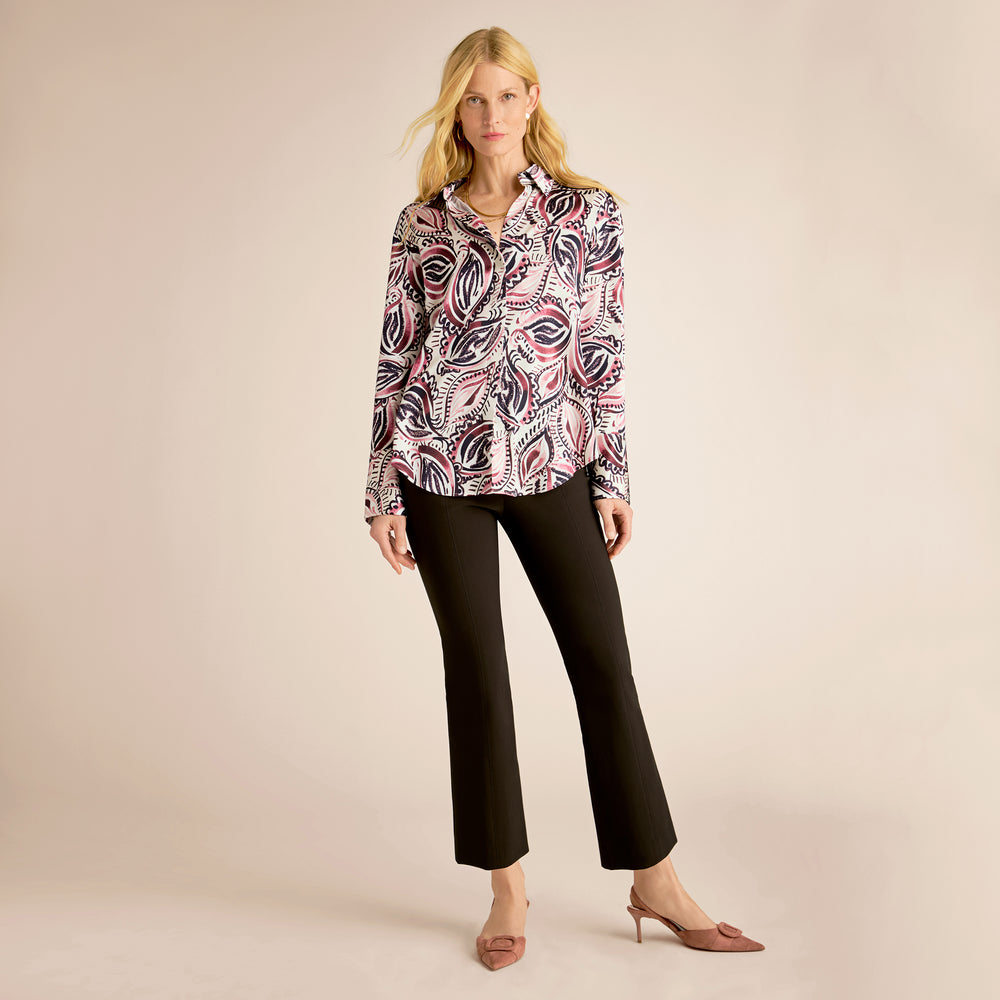 Woman wearing a patterned blouse and black pants on a beige background