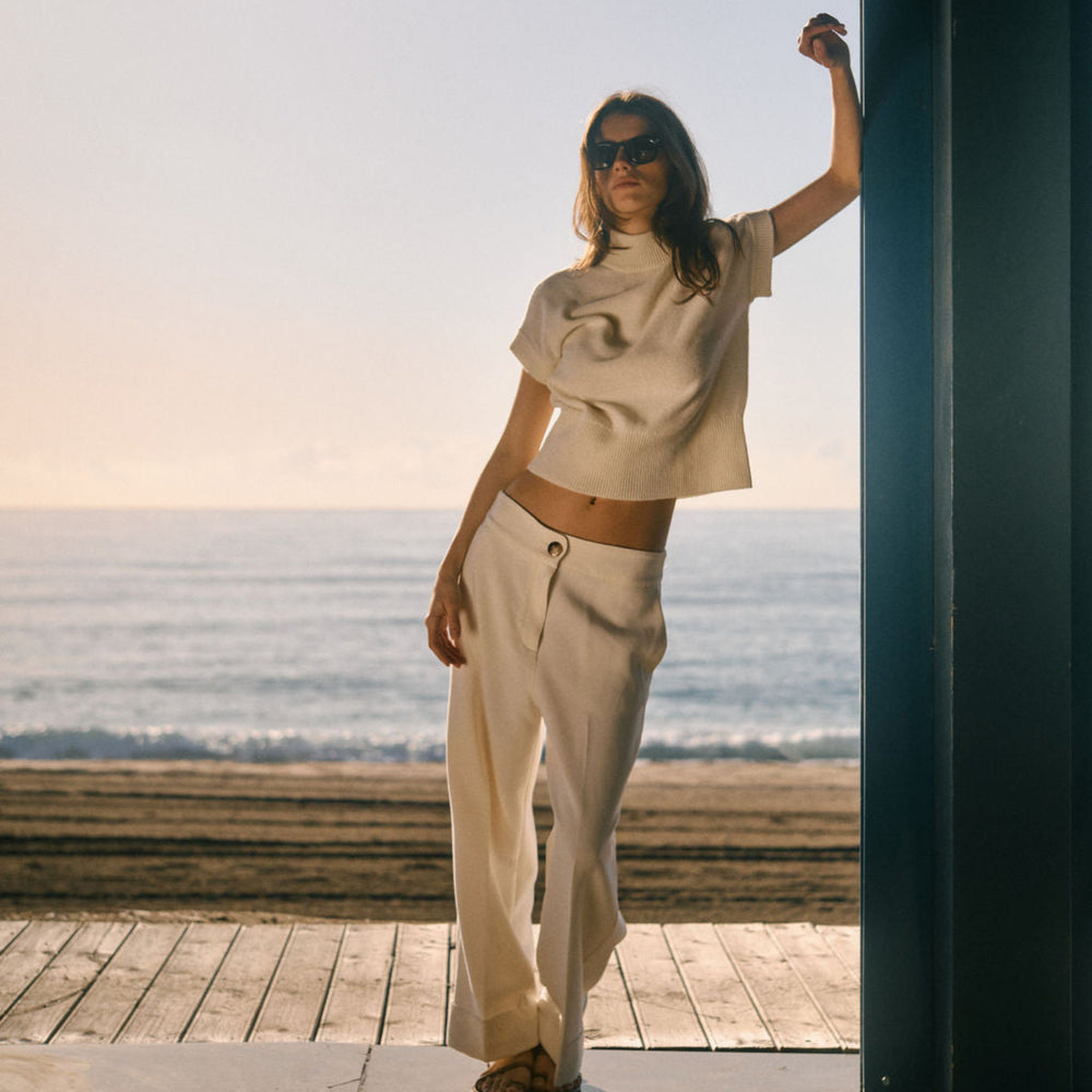 Woman standing on a wooden deck by the ocean with a clear sky.