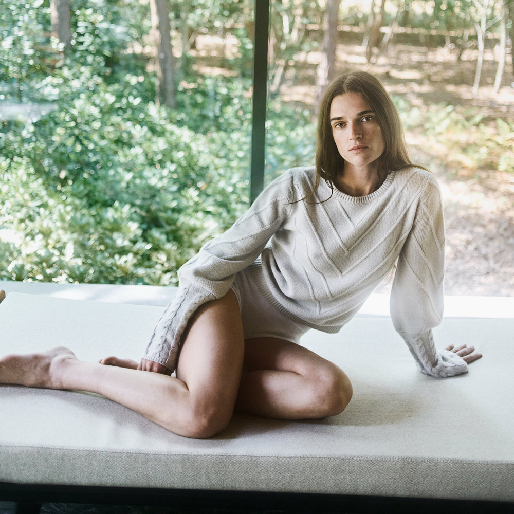 Woman sitting on a couch in a room with large windows showing a forest view