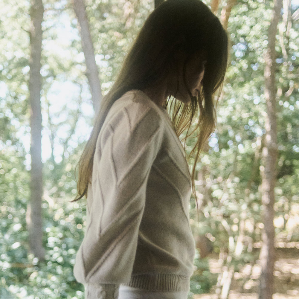 Person wearing a beige sweater and white shorts standing in front of a forest view.