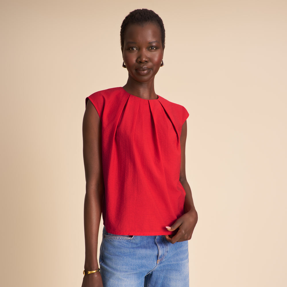 Woman wearing a red sleeveless top and blue jeans on a beige background