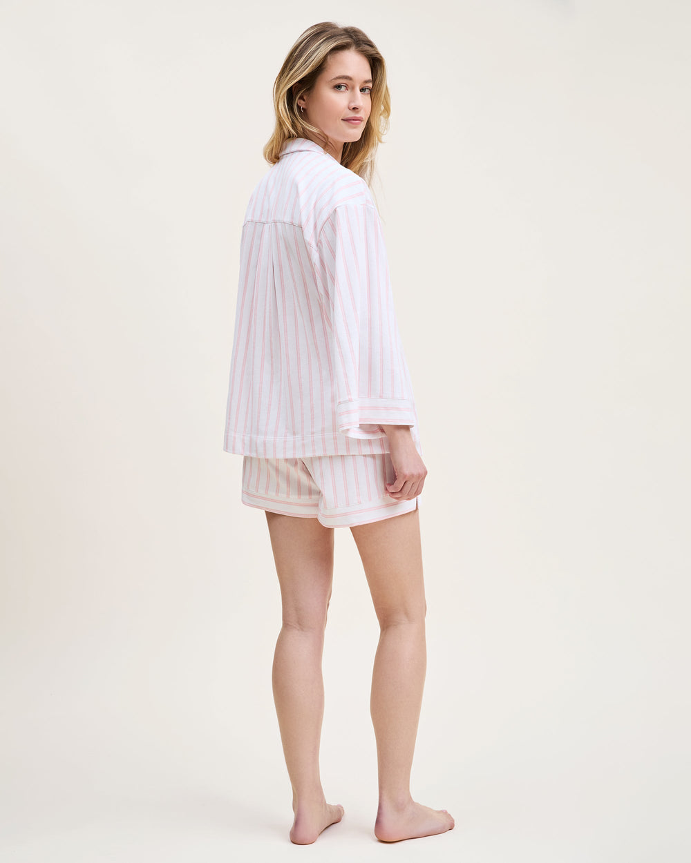 Woman wearing a white striped shirt and shorts on a plain background