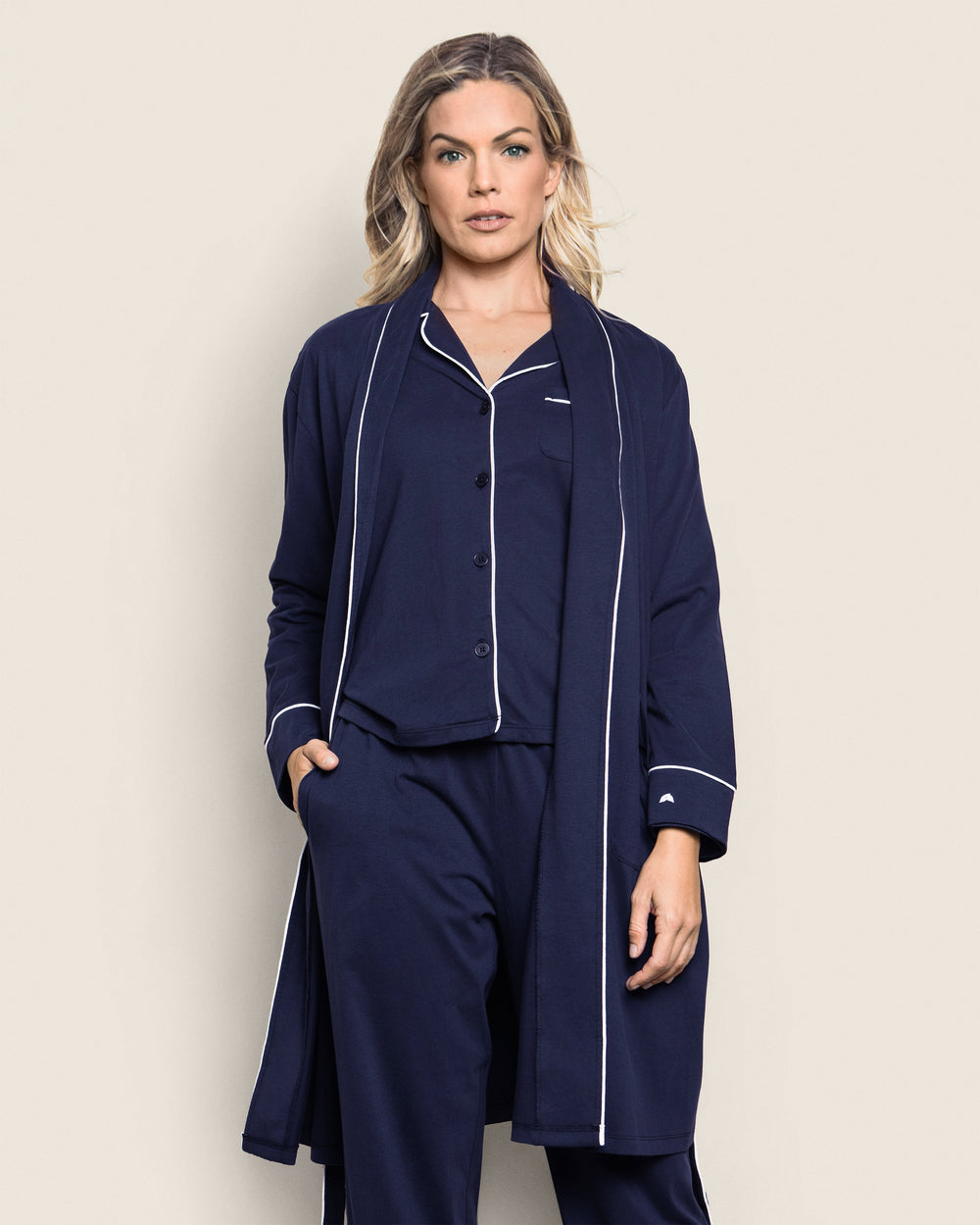 Woman wearing a navy blue pajama set with white piping on a beige background