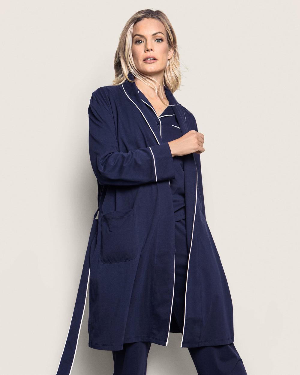 Woman wearing a navy blue robe with white piping on a plain background