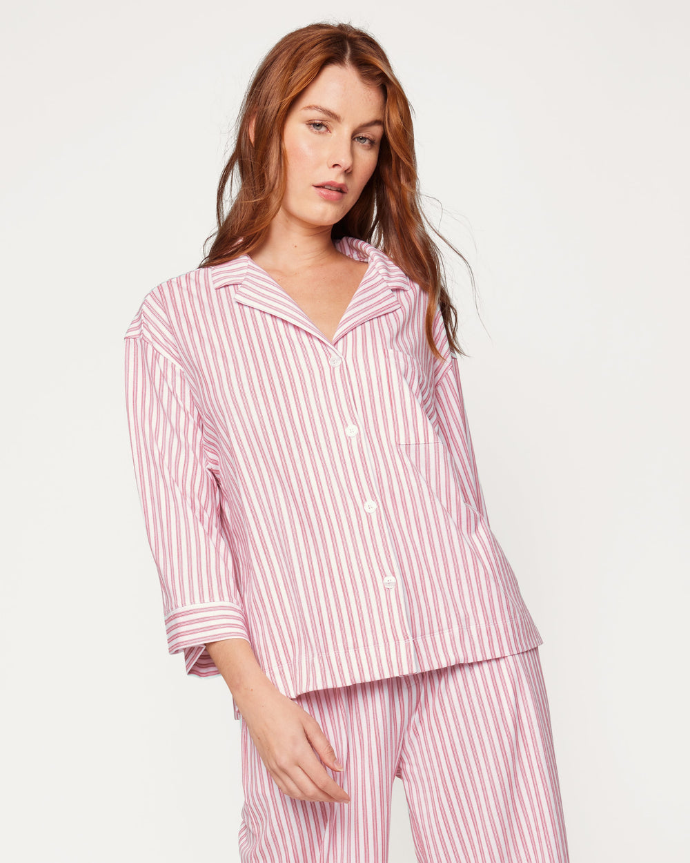 Woman wearing a pink and white striped pajama set on a light gray background