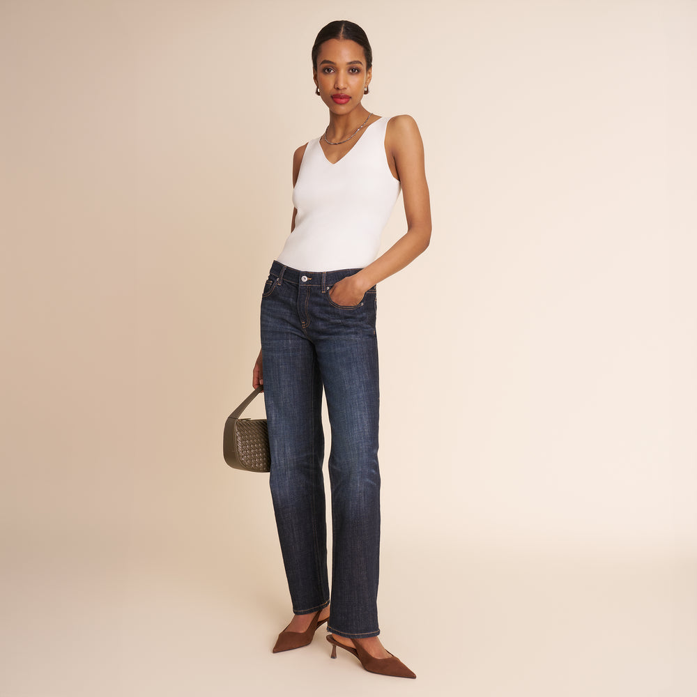 Woman wearing a white sleeveless top and blue jeans on a beige background